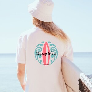 May include: White t-shirt with a pink and blue surfboard graphic and the text "Chasing Waves".