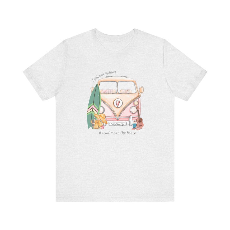 May include: A light grey t-shirt with a pink and white vintage van with a surfboard and a guitar. The text on the shirt reads "I followed my heart, it lead me to the beach." and "Salty Soul Life"