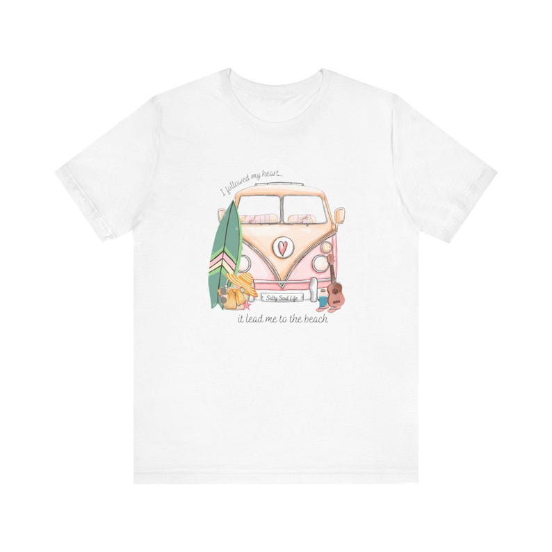May include: White t-shirt with a pink and white vintage van illustration. The van has a surfboard, a guitar, and a suitcase on the side. The text "I followed my heart, it lead me to the beach" is printed below the van. The text "Salty Soul Life" is printed on the van.