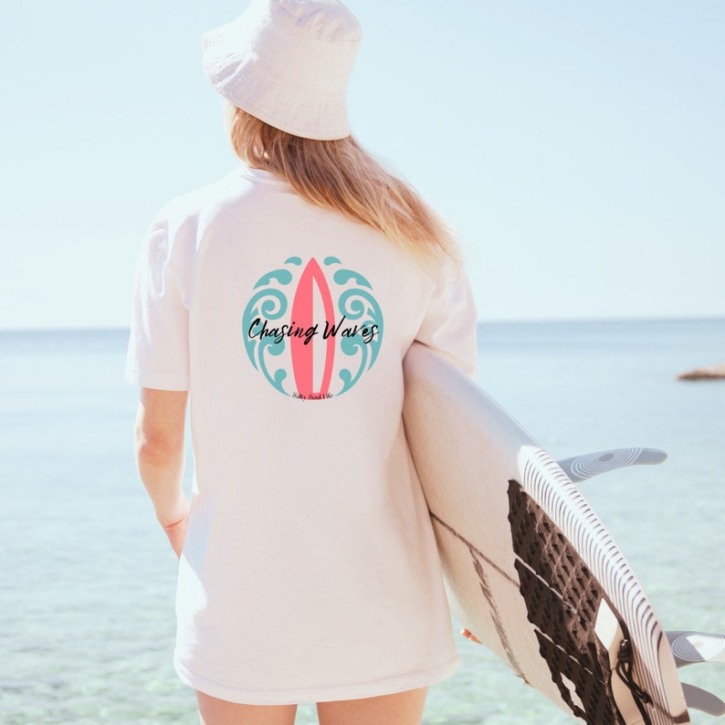 May include: White t-shirt with a pink and blue surfboard graphic and the text "Chasing Waves".
