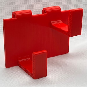 May include: A red plastic wall-mounted hook with two hooks. The hooks are designed to hold items like coats, hats, or bags.