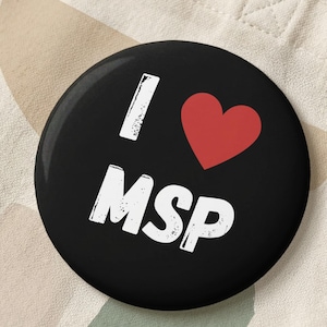 May include: A black button with the text "I ❤️ MSP" in white, with a red heart symbol. The button is on a beige tote bag with a colorful abstract design.
