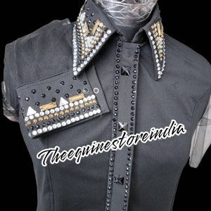 Pu&ograve; includere: Camicia nera senza maniche con colletto e polsini tempestati di strass. Il colletto presenta un design geometrico con accenti dorati. La camicia ha il testo "Thee equineststore india" stampato sul davanti.