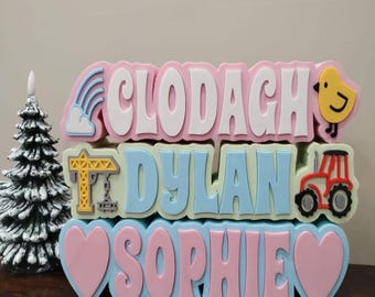 May include: Three personalized wooden blocks with names "Clodagh", "Dylan", and "Sophie" in white letters. The blocks are decorated with a rainbow, a cloud, a yellow chick, a construction crane, a red tractor, and pink hearts.