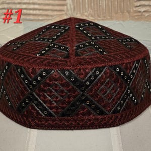 May include: A burgundy-colored, embroidered skullcap with a geometric pattern. The hat features black and silver accents, with the number "#1" in red at the top. The design includes diamond and cross-shaped patterns.