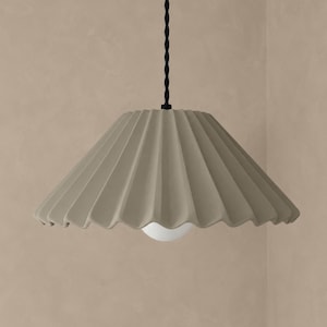 May include: A taupe-colored pendant light fixture featuring a wide, pleated, conical shade. The lamp is suspended by a black twisted cord and includes a single, round, white light bulb visible at the center of the shade's opening.