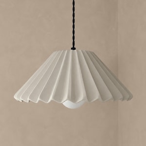 May include: A pendant light featuring a wide, beige, pleated lampshade with a conical shape. The shade is suspended by a thin, black, twisted cord. A small, round, white light bulb is visible at the center of the bottom opening of the shade.