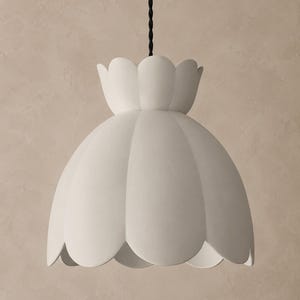 Può includere: Una lampada a sospensione bianco opaco caratterizzata da un paralume smerlato a forma di fiore. La lampada è appesa a un cavo in tessuto intrecciato nero e presenta una silhouette liscia e curva che si allarga verso il bordo inferiore.