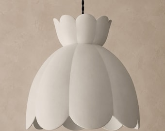 May include: A matte white pendant light fitting featuring a scalloped, flower-like shade design. The lamp is suspended from a black twisted fabric flex. The shade has a wide, rounded bottom edge and a smaller, upright scalloped collar at the top.