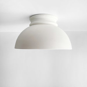 Op de afbeelding: Een witte plafondlamp met een koepelvormige kap en een decoratieve basis.