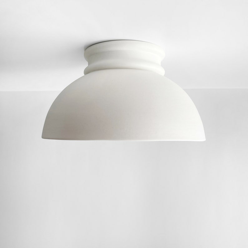 Op de afbeelding: Een witte plafondlamp met een koepelvormige kap en een decoratieve basis.