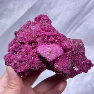 May include: A vibrant magenta-colored mineral specimen with a rough, crystalline, and porous texture. The rock features an irregular, jagged shape with a prominent heart-shaped protrusion on its front surface, displaying deep pink hues.