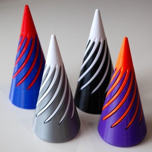 Puede incluir: Cuatro objetos decorativos en forma de cono de varios colores. Cada cono tiene una punta blanca y una base azul, gris, negro y morado. Los conos presentan un diseño en espiral en colores contrastantes, como rojo sobre azul y naranja sobre morado.