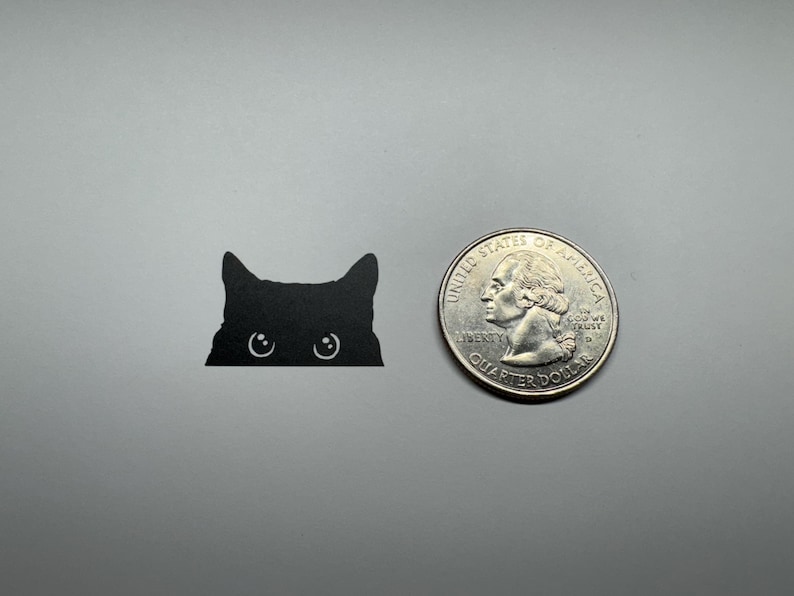 May include: A black cat silhouette with large eyes peeking over a surface. The cat is about the size of a US quarter.