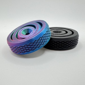 May include: Two decorative, circular objects. One is a gradient of blue, purple, and green, with a textured, diamond-patterned exterior. The other is black with a similar diamond pattern. Both have a spiral design.