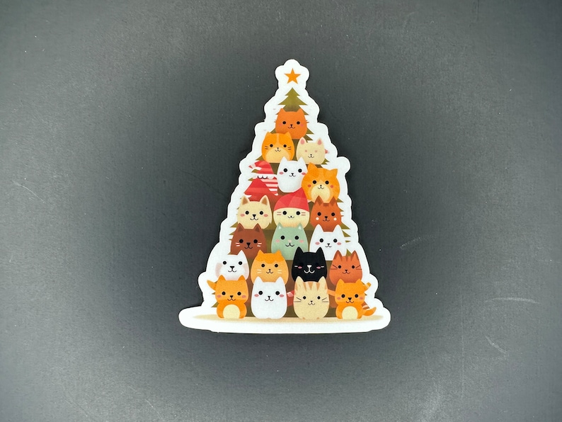 May include: A sticker of a Christmas tree made of cats. The cats are all different colors and have different expressions on their faces. There is a star on top of the tree.
