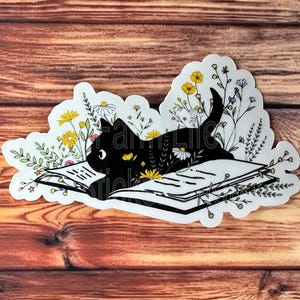May include: A black cat reading a book surrounded by yellow and white flowers. The cat is lying on its side with its head resting on the book. The book is open and the pages are visible. The flowers are arranged around the cat and the book.