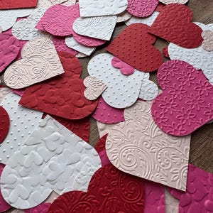 May include: A collection of red, pink, and white paper hearts with various embossed patterns. The hearts are arranged in a random pattern, overlapping each other.