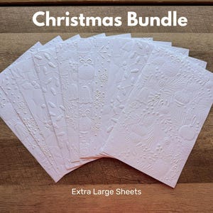 May include: A collection of white rectangular sheets featuring embossed Christmas-themed patterns including ornaments, snowflakes, bells, and string lights. The text "Christmas Bundle" and "Extra Large Sheets" is printed on the image.