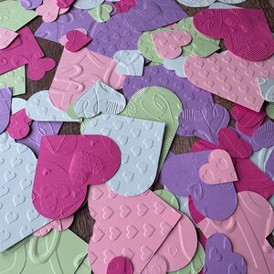 May include: A collection of paper hearts in various shades of pink, purple, and green. The hearts are embossed with different patterns, including small hearts, swirls, and leaves.