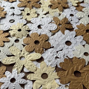 May include: Assortment of paper flowers in white, cream, and gold. The flowers have a variety of embossed patterns and are perfect for crafting or decorating.