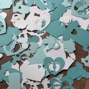 May include: A collection of teal and white paper cutouts in various shapes, including hearts, footprints, and onesies. The cutouts are scattered on a wooden surface.