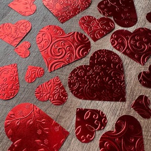 May include: A collection of red foil hearts with intricate embossed designs. The hearts are various sizes and shapes, perfect for crafting or decorating.