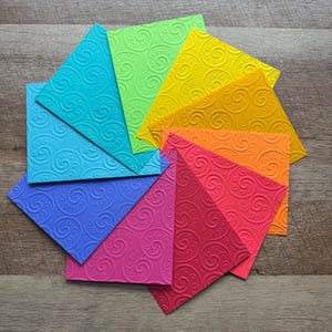 May include: A rainbow of colorful patterned paper squares arranged in a circular pattern. The squares are all the same size and have a swirling pattern.
