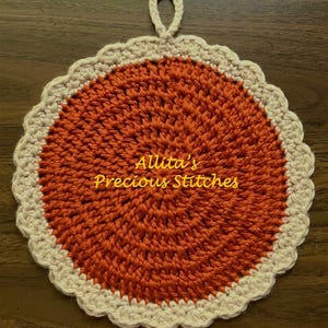 May include: A crocheted orange and cream pot holder with a loop handle. The pot holder has a scalloped edge and the text "Allita's Precious Stitches" is in the center.