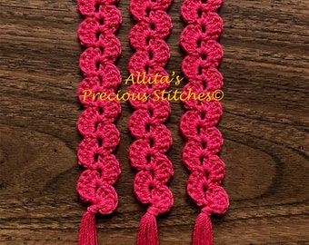 May include: Three handmade, bright pink crochet bookmarks with a floral design and tassel ends. The text "Allita's Precious Stitches" is visible in the image. The bookmarks are displayed on a wooden surface.