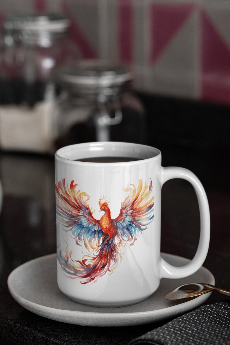 May include: White ceramic coffee mug featuring a colourful phoenix design. The phoenix is depicted with red, orange, yellow, blue, and purple feathers. The mug is filled with coffee and resting on a white saucer.