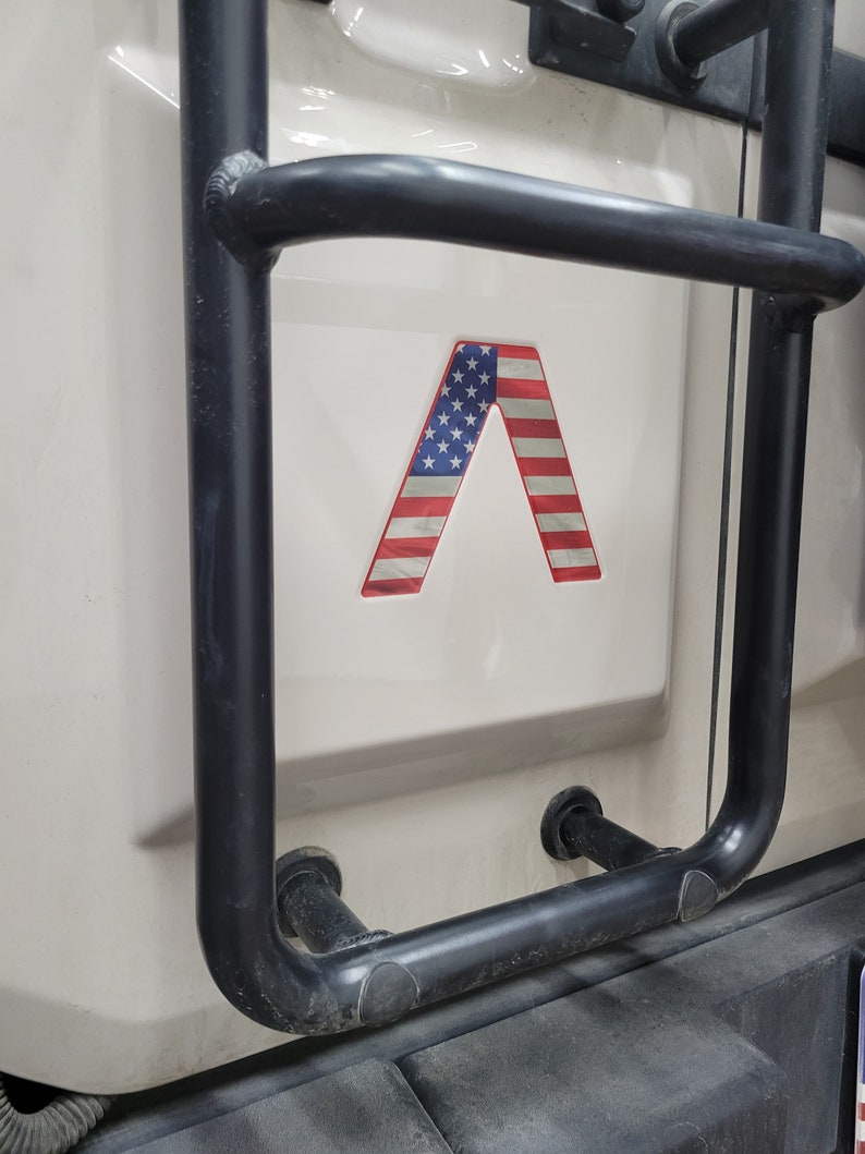 May include: A black metal ladder rack with a red, white, and blue American flag decal in the shape of a letter A.