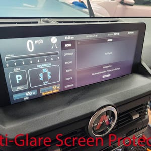 May include: A black car dashboard with a digital display showing the speed, gear, and other information. The display also shows the time, temperature, and audio settings. The car is a Grenadier, a new off-road vehicle.