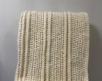 May include: A cream-coloured crocheted throw blanket with a ribbed texture. The blanket is folded and draped over a chair.