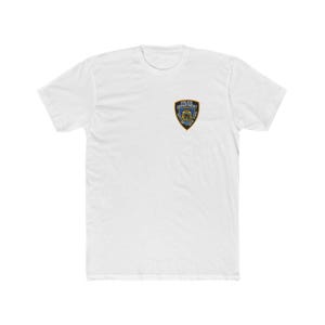 Peut inclure: T-shirt blanc avec un petit écusson de la Police sur la poitrine gauche. L'écusson a une bordure bleue, des accents dorés et les mots "Police Department City of New York". Le t-shirt est fait d'une matière douce et confortable.