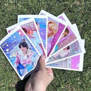 Puede incluir: Un conjunto de siete tarjetas de fotos coloridas con diferentes miembros del grupo de K-pop Stray Kids. Cada tarjeta tiene la foto de un miembro diferente con su nombre y el nombre del grupo escrito en ella. Las tarjetas están decoradas con corazones, estrellas y otros diseños lindos.