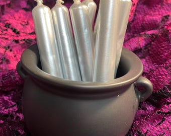 May include: A black cauldron filled with silver taper candles. The cauldron is sitting on a purple lace fabric.