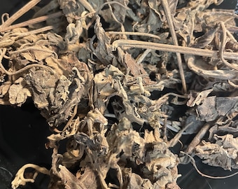 May include: Dried herbs in a black bowl. The herbs are brown and have a rough texture.