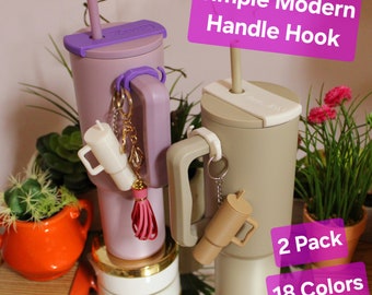 May include: Two stainless steel tumblers with a modern handle hook attachment. The tumblers are in a light purple and a light brown color. The text "Simple Modern Handle Hook" and "2 Pack 18 Colors" is visible in the image.