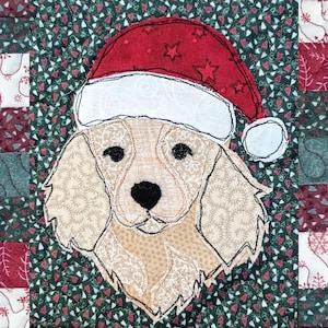 Peut inclure: Décoration de Noël matelassée avec un chien portant un bonnet de Père Noël. Le visage du chien est beige avec des yeux et un nez noirs, soulignés de coutures noires. Le chapeau est rouge avec une bordure blanche et des étoiles.