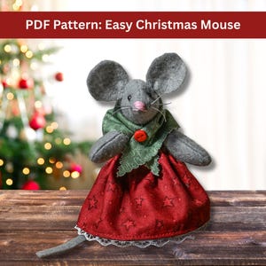 May include: A gray felt mouse doll wearing a green scarf and a red dress with white lace trim. The dress has a star pattern. The text "PDF Pattern: Easy Christmas Mouse" is at the top of the image.