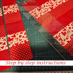 May include: Red and white fabric strips with heart and polka dot patterns are arranged on a green cutting mat. A clear ruler is positioned diagonally across the fabric. The text "Step by step instructions" is at the bottom.