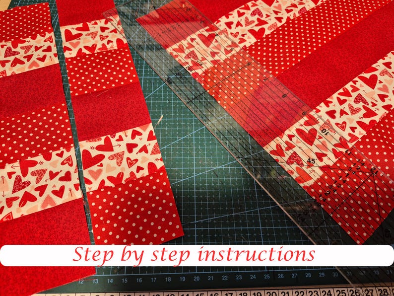 May include: Red and white fabric strips with heart and polka dot patterns are arranged on a green cutting mat. A clear ruler is positioned diagonally across the fabric. The text "Step by step instructions" is at the bottom.