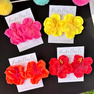 May include: Four pairs of polymer clay earrings in vibrant colors: hot pink, yellow, orange, and red. Each pair is shaped like a hibiscus flower and displayed on a white card with the text "Bonita Clay Co" and "Polymer Clay Earrings".