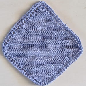 Peut inclure: Un gant de toilette tricoté à la main, en forme de losange, de couleur bleu pervenche clair. Le gant de toilette présente un motif texturé avec des rayures horizontales et une bordure ajourée décorative. L'article est en fil doux, peut-être en coton.