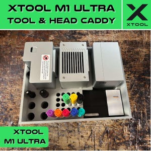 Può includere: Un caddy grigio per strumenti e teste con il testo "XTOOL M1 ULTRA TOOL & HEAD CADDY" in alto. Il caddy ha un vano per gli strumenti e un vano per i pennarelli. Il caddy è in plastica e ha un interno bianco.