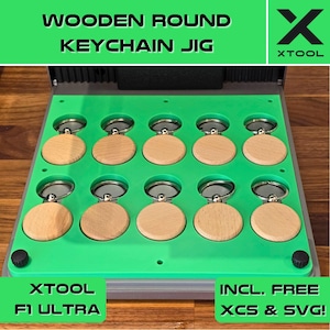 Op de afbeelding: Een groene en grijze houten sleutelhangerjig met 12 ronde sleuven voor het maken van sleutelhangers. De jig is gelabeld "XTOOL F1 ULTRA" en "INCL. FREE XCS & SVG!"