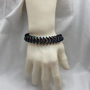 May include: A black chainmail bracelet with iridescent rainbow coloring. The bracelet is made of small metal rings linked together.