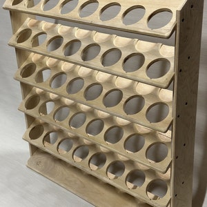 May include: A wooden shelf unit with six tiers, each tier has 10 circular cutouts for storing items. The shelf unit is made of light brown wood and has a natural finish.