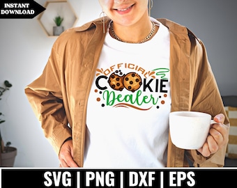 May include: A white t-shirt with the text "Official Cookie Dealer" in green, black, and brown lettering. The text is surrounded by a green swirl and two brown chocolate chip cookies.
